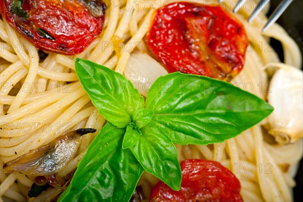 Italian spaghetti pasta with baked tomatoes basil and thyme sauce on a cast iron skillet