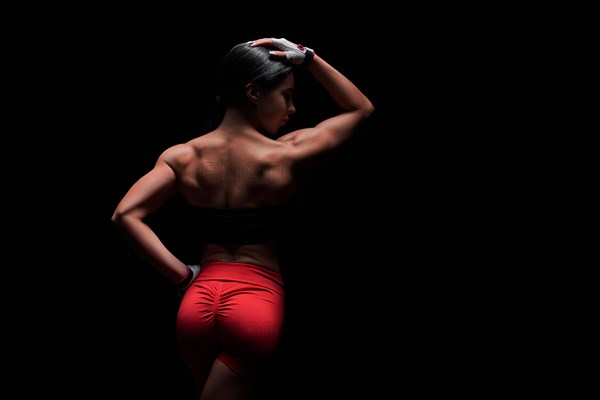 Athletic young woman showing back and arm muscles on isolated black background. Mixed media