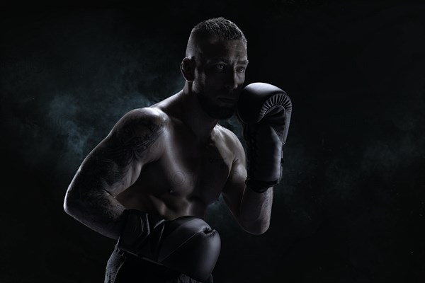 Kickboxer in black gloves posing on a background of smoke. The concept of mixed martial arts. MMA