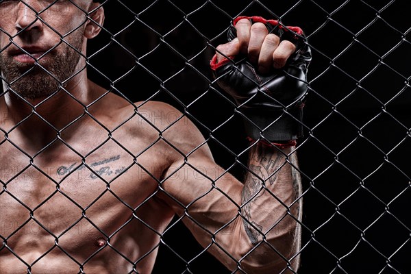 Dramatic image of a mixed martial arts fighter standing in an octagon cage. The concept of sports