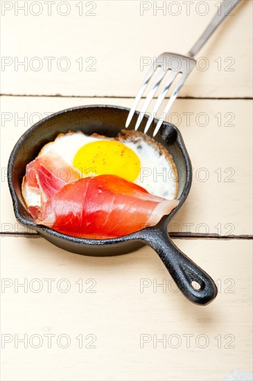 Fried egg sunny side up with Italian tyrolean speck smoked ham on a skillet