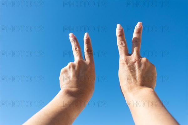 Woman's hands showing sign of victotia against blue sky background