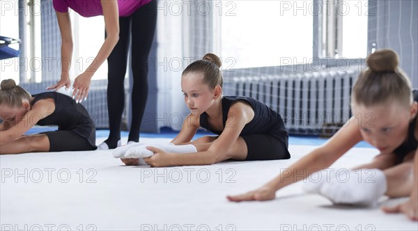 A group of three little girls train on a white mat in a sports club. Gymnastics concept. Mixed media