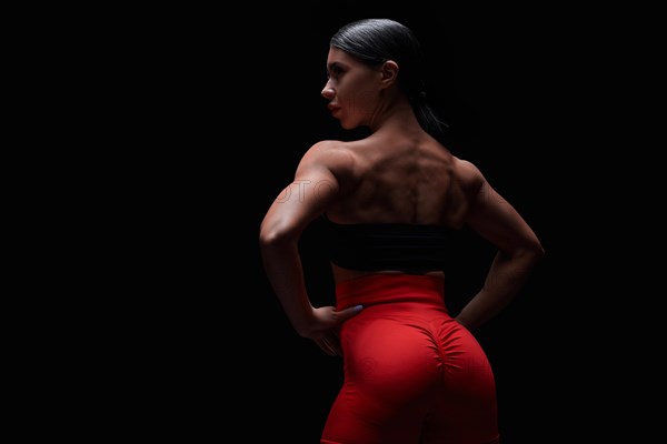 Athletic young woman showing back and arm muscles on isolated black background. Mixed media