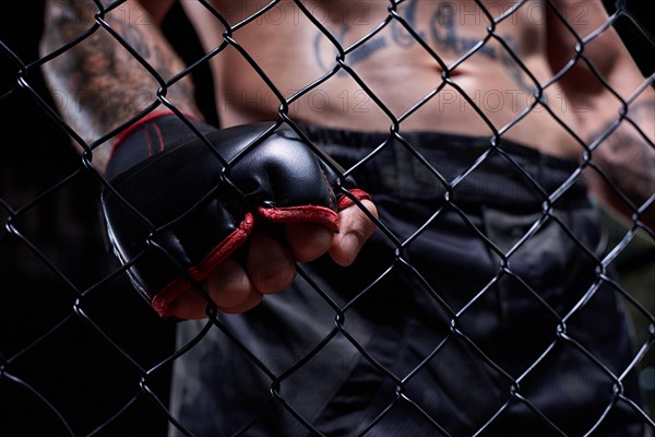 Dramatic image of a mixed martial arts fighter standing in an octagon cage. Powerful abdominal muscles. The concept of sports