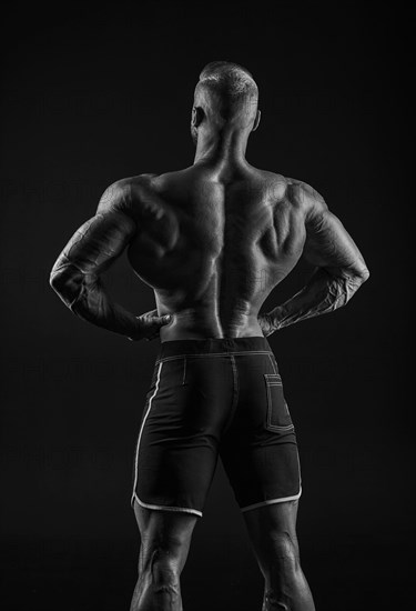 Silhouette of a strong bodybuilder. View from the back. Confident young fitness athlete with a powerful body and perfect abs. Black and white photography. Dramatic light