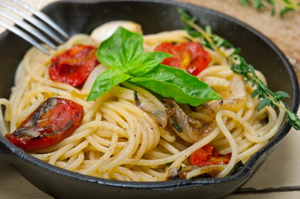 Italian spaghetti pasta with baked tomatoes basil and thyme sauce on a cast iron skillet