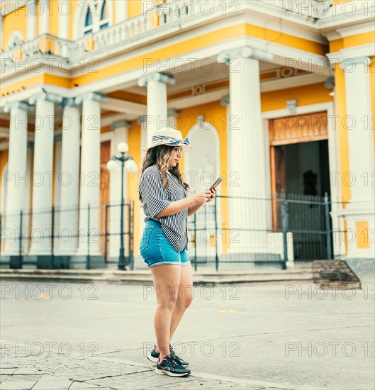 Lifestyle of tourist woman texting with phone on the street of square. Beautiful young travel woman with hat using cell phone on the street of Granada Nicaragua
