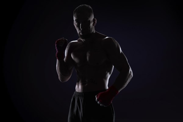 Kickboxer in red bandages posing on a blue background. The concept of mixed martial arts. MMA