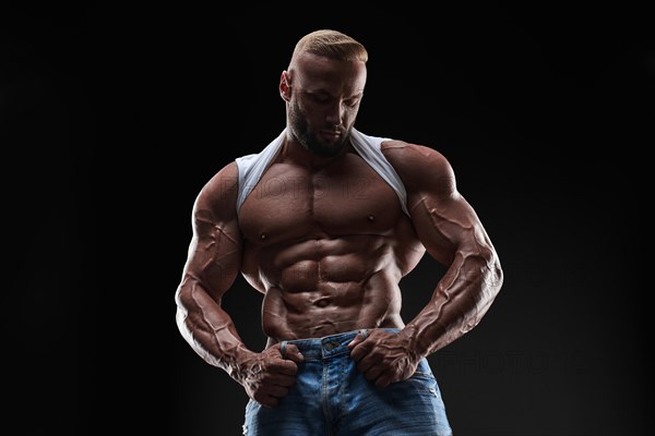 Muscular model man in white t-shirt on a black background. Sporty guy showing his big shoulders