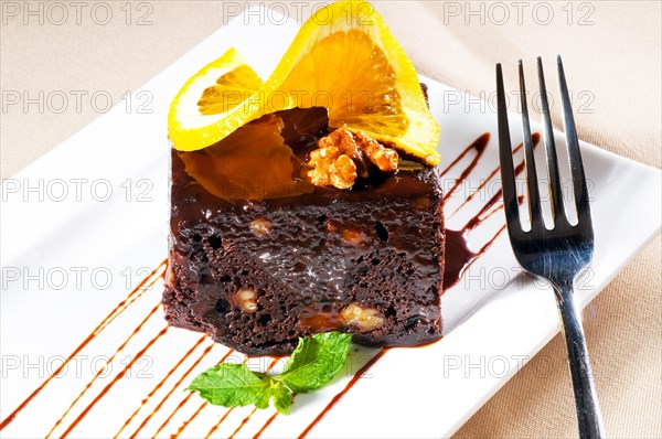 Fresh baked delicious chocolate and walnuts cake with slice of orance on top and mint leaf