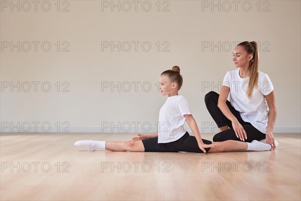 Beautiful female teacher helps a little girl stretch in a gymnastics class. The concept of education