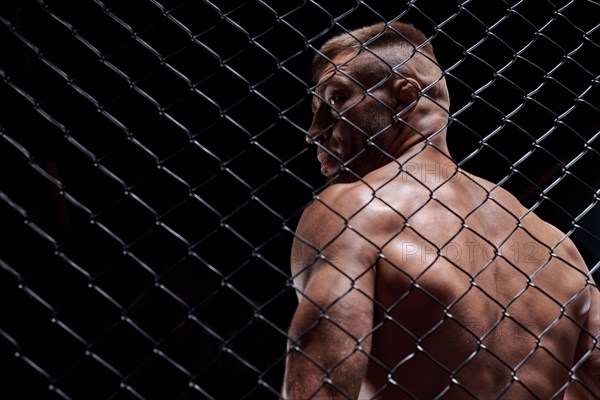 Dramatic image of a mixed martial arts fighter standing in an octagon cage. The concept of sports