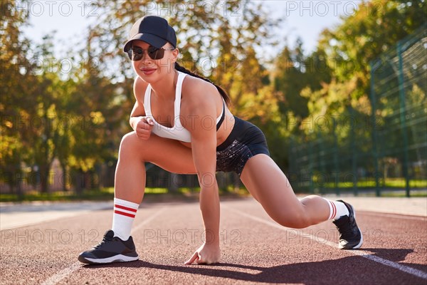 Beautiful young fitness girl is warming up at the stadium before training. Attractive slim brunette in a tracksuit