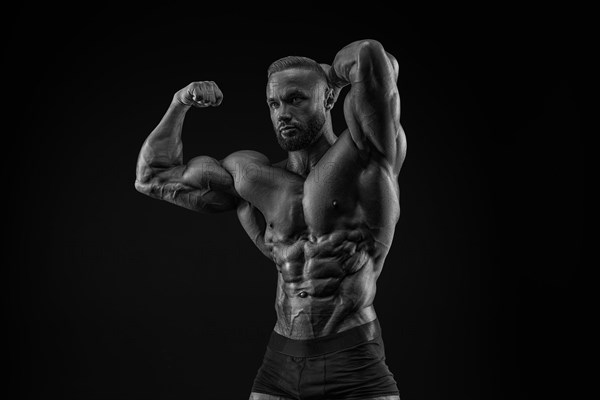 Silhouette of a strong bodybuilder. Confident young fitness athlete with a powerful body and perfect abs. Black and white photography. Dramatic light. Mixed media