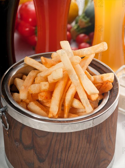 Fresh french fries on a wood bucket with selection of beers and fresh vegetables on background