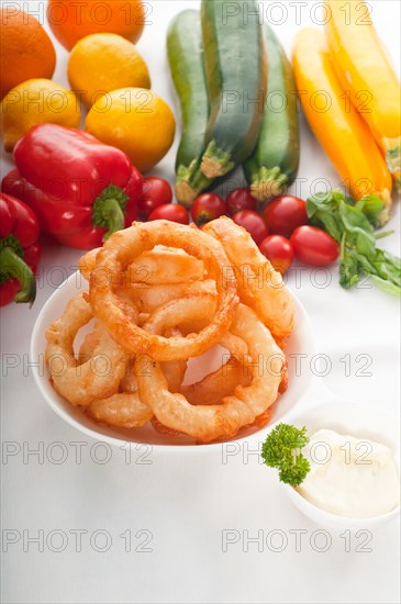 Golden deep fried onion rings served with mayonnaise dip and fresh vegetables oln background