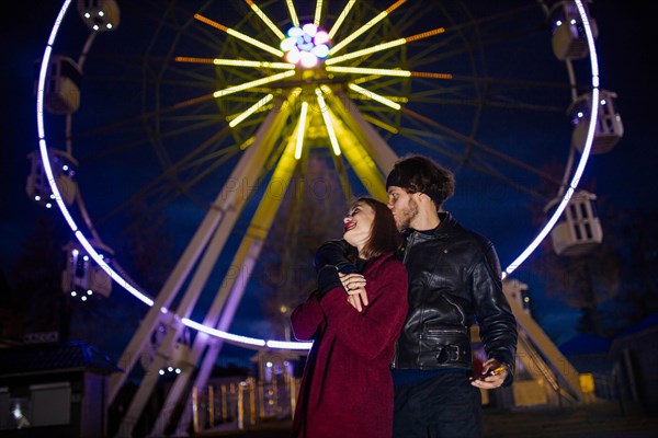 Couple in love in an amusement park near a ferris wheel on a date in cold weather. The concept of love and joy in relationships