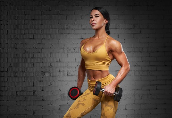 Sexy fitness woman. A beautiful athletic girl posing in the studio in a yellow training suit against the background of a brick wall. Sports and fitness concept