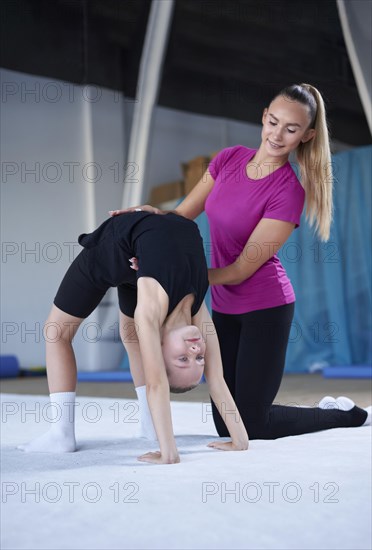 Training in the gym class. A little girl under the guidance of a trainer performs exercises. Gymnastics concept. Mixed media