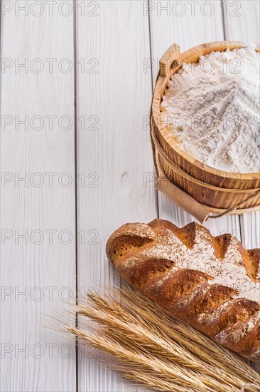 Loaf of bread Wheat ears Flour in wooden bucket on old white boards with copy space