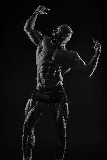 Silhouette of a strong bodybuilder. Confident young fitness athlete with a powerful body and perfect abs. Black and white photography. Dramatic light. Mixed media