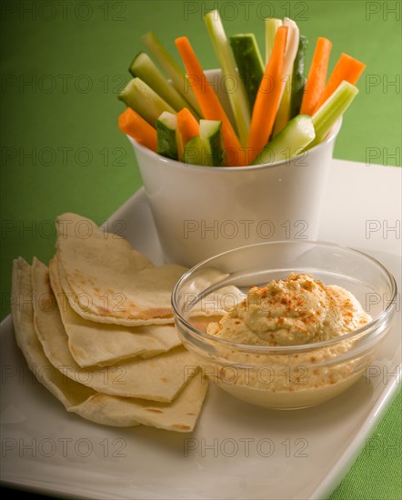 Middle eastern hummus dip on a glass bowl with homemade pita bread and raw vegetable