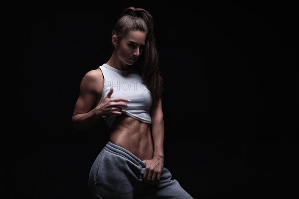 Athletic fitness woman posing in the studio on a dark background. Photo of an attractive woman in fashionable sportswear. Sports and healthy lifestyle. Mixed media