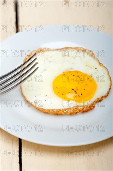 Fried egg sunny side up on a plate with fork over wood table