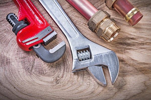 Copper water pipe wrench nipple hose connectors adjustable spanner on wooden board top view plumbing concept