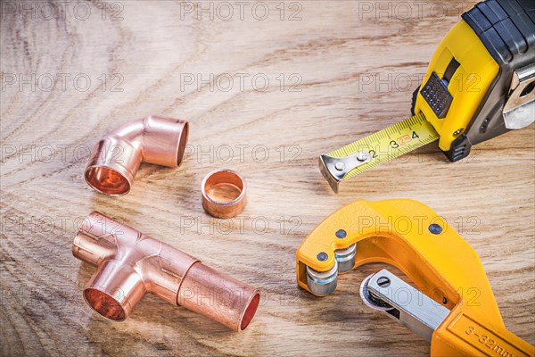 Composition of brass pipe cutter fittings measuring tape on wooden board plumbing concept