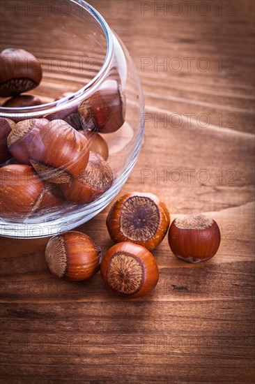 Hazelnuts and transparent round glass bowl on vintage wooden board Food and drink still life