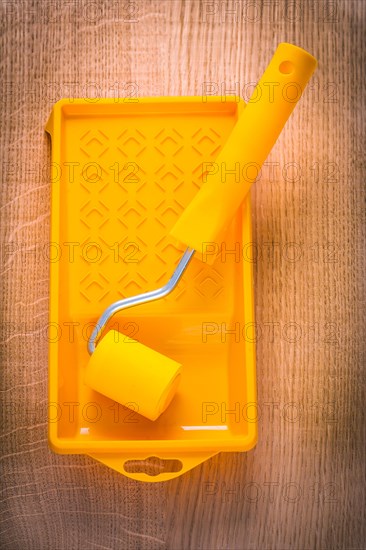 Yellow paint roller in bowl on wooden board