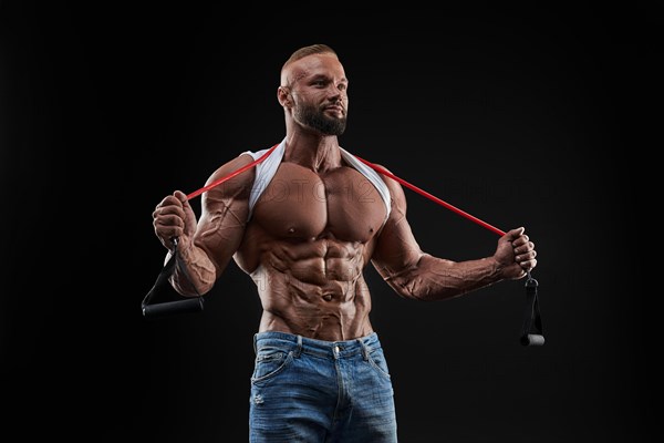 Muscular guy stretching rubber resistance bands in dark background. Perfect body. Mixed media