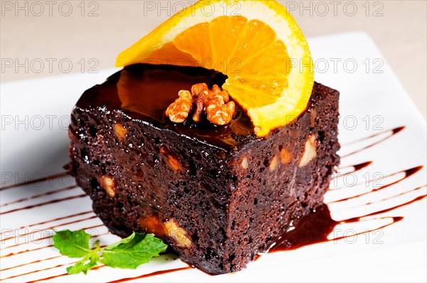 Fresh baked delicious chocolate and walnuts cake with slice of orance on top and mint leaf