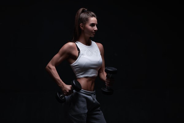 Athletic fitness woman posing in the studio on a dark background. Photo of an attractive woman in fashionable sportswear. Sports and healthy lifestyle. Mixed media