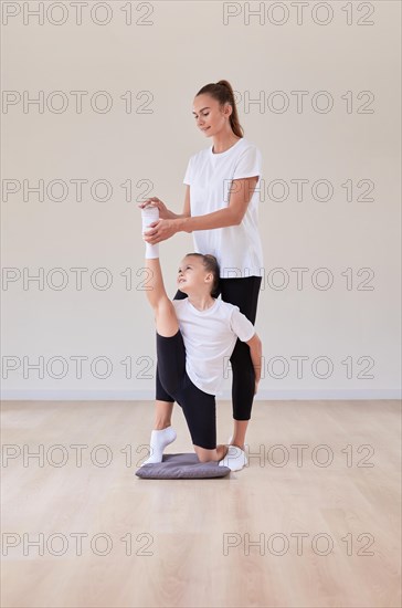 Beautiful female teacher helps a little girl stretch in a gymnastics class. The concept of education