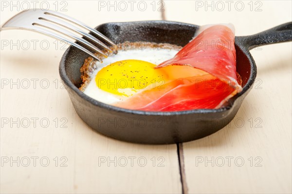 Fried egg sunny side up with Italian tyrolean speck smoked ham on a skillet