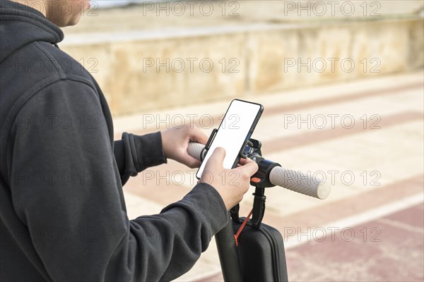 Top side view 14-20 years old riding scooter using mobile phone navigation route outdoors in nature