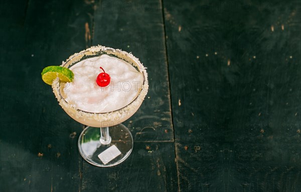 Coconut margarita with cherry on wooden table. Frozen coconut cocktail with cherry on top on wooden table