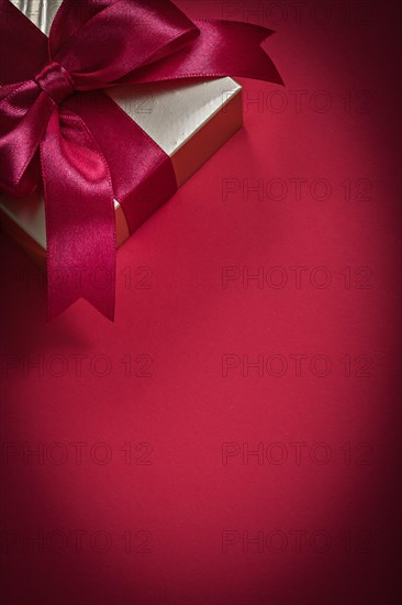 Wrapped giftbox with tied bow on red background holidays concept