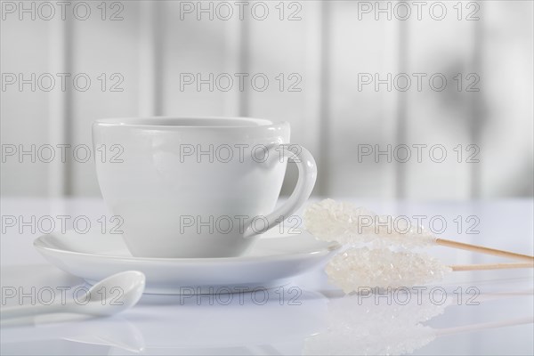 A coffee cup with spoon and candy cane on a white table