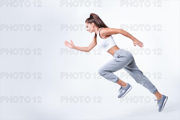 Sports woman runner on a white background. Photo of an attractive woman in fashionable sportswear. Dynamic movement. Side view. Sports and healthy lifestyle. Mixed media