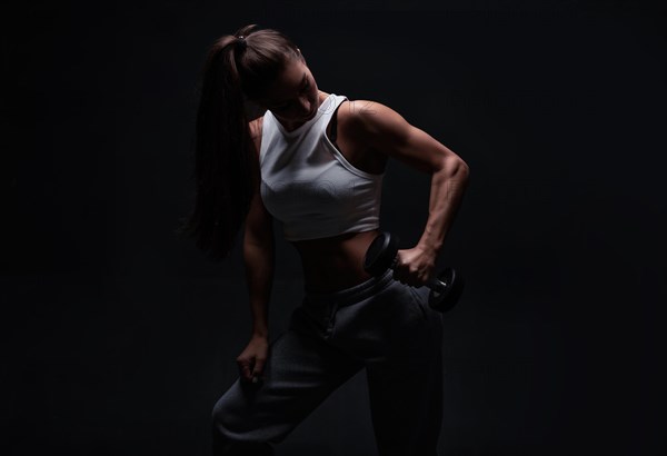 Athletic fitness woman posing in the studio on a dark background. Photo of an attractive woman in fashionable sportswear. Sports and healthy lifestyle. Mixed media