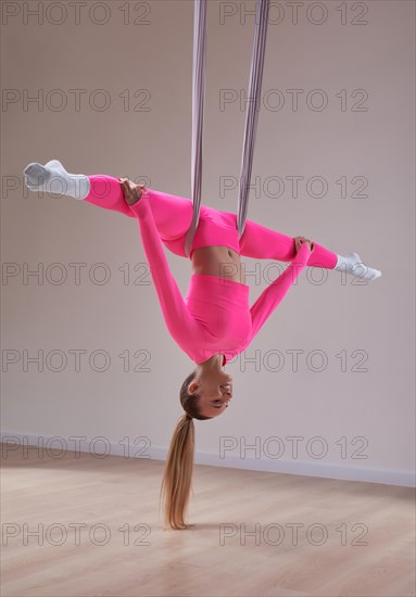 Image of a beautiful woman posing in a bright studio near the hammocks. The concept of airstretching. Fitness and sports