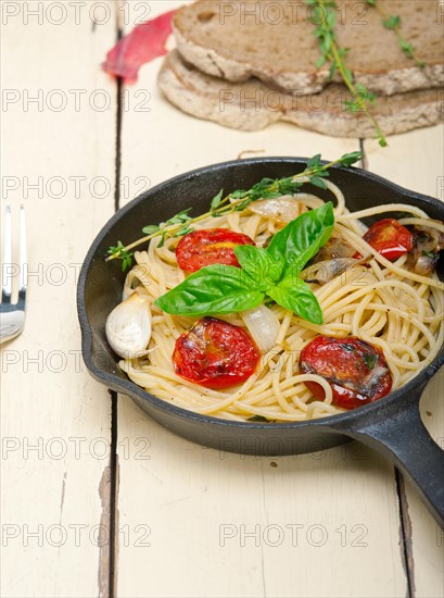 Italian spaghetti pasta with baked tomatoes basil and thyme sauce on a cast iron skillet