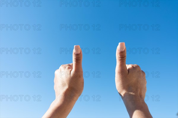 Woman's hands showing thumbs on a blue sky background