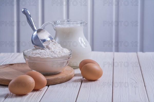 Composition bowl with flour scop eggs milk in pitcher on white painted old wooden board food and drink concept