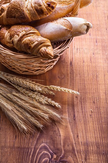 Close-up of baguettes and croissants in a wicker basket with ears of wheat