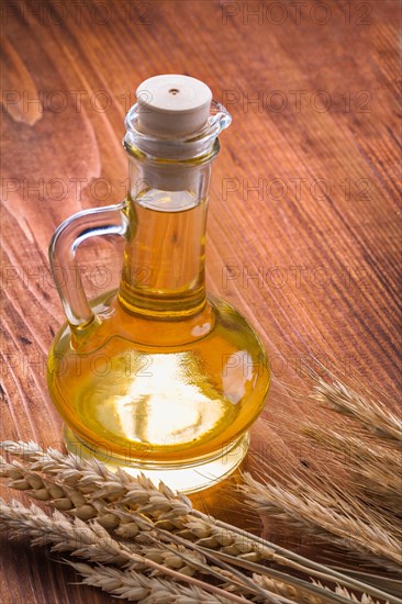 Oil bottle with ears of wheat on old wooden boards